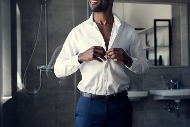 tiro recortado de homem de negócios sorridente abotoando sua camisa branca no banheiro
 - Foto, Imagem