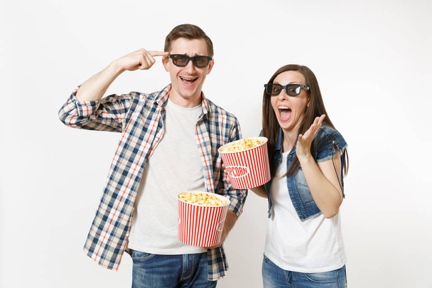 Fiatal pár őrült, nő és férfi 3D-s szemüveg és alkalmi ruhák, néz film film napon gazdaság vödrök a pattogatott kukorica, nevetve a elszigetelt fehér háttér. Érzelmek a mozi koncepció - Fotó, kép