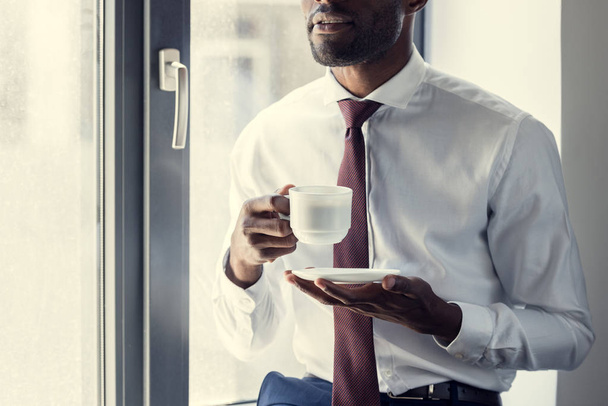 cropped shot of young businessman with cup of coffee in front of window - Foto, immagini