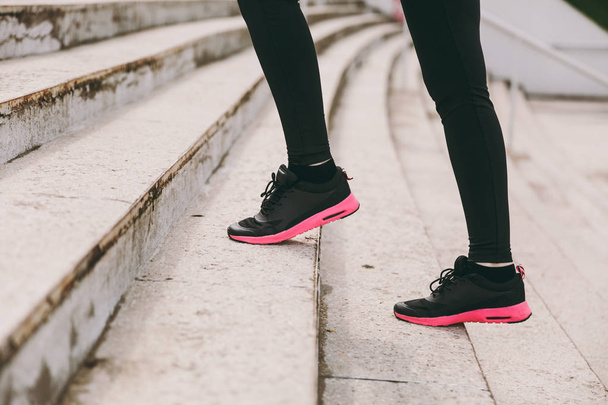 Cropped photo close up of female legs in sportswear, black and pink woman sneakers doing sport exercises, climbing on stairs outdoors. Fitness, healthy lifestyle concept. Copy space for advertisement - Photo, Image