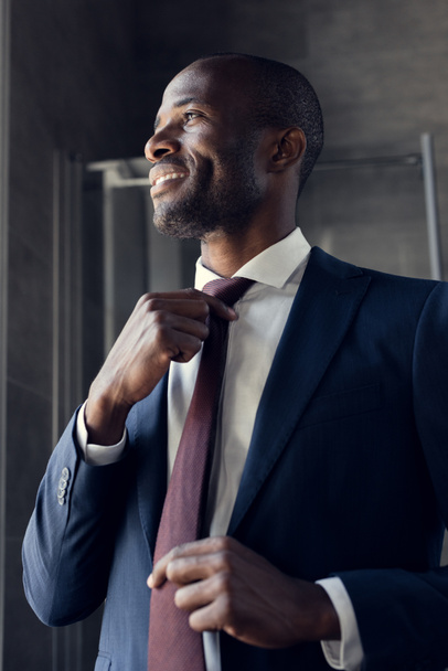 glücklicher junger Geschäftsmann zieht Krawatte an und schaut weg - Foto, Bild