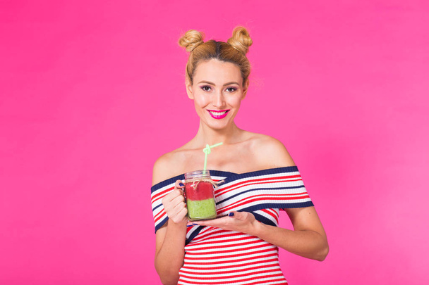 Primer plano retrato de estudio de la mujer joven divertida con traje brillante, sosteniendo y bebiendo sabroso batido verde batido sobre fondo rosa
 - Foto, imagen