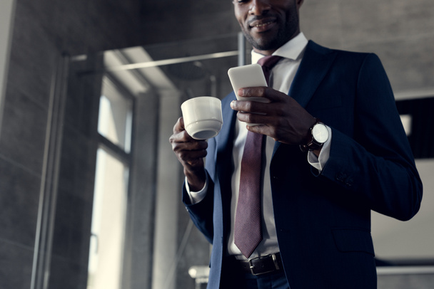 bottom view of handsome young businessman with cup of coffee using smartphone in bathroom - Foto, Imagem