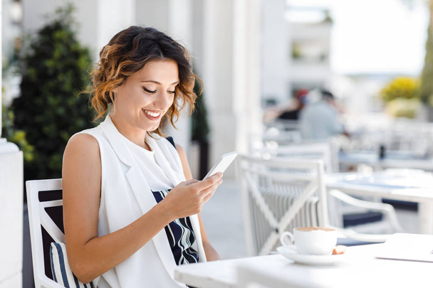 Docela kavkazská, usmívající se žena sedí v kavárně a textových zpráv na mobilním telefonu. - Fotografie, Obrázek