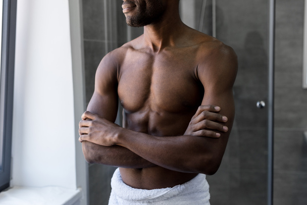 Oříznout záběr úsměvem afroamerické muže v postavení ručník s překřížením rukou v koupelně - Fotografie, Obrázek