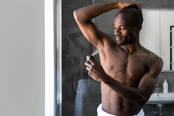 sonriente afroamericano hombre en toalla sosteniendo desodorante spray en baño
 - Foto, Imagen