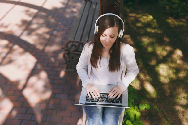 junge erfolgreiche Geschäftsfrau in leichter Freizeitkleidung. Frau arbeitet an modernem Laptop-PC, hört Musik über Kopfhörer auf der Straße im Freien. mobiles Büro. freiberufliches Geschäftskonzept - Foto, Bild