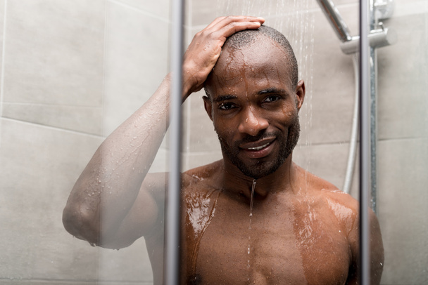 guapo afroamericano hombre tomando ducha y sonriendo a la cámara
 - Foto, imagen