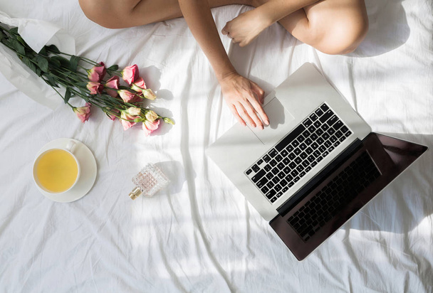 Cropped unrecognisable woman sitting on her bed in the morning and typing on her laptop. - Фото, зображення