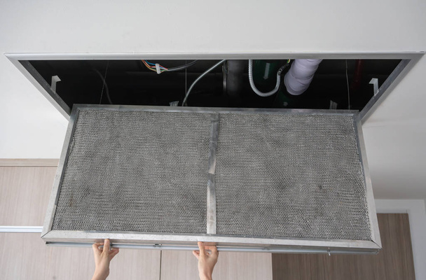 Mano llegando hasta soporte de filtro abierto para filtro de aire acondicionado en el techo
 - Foto, imagen