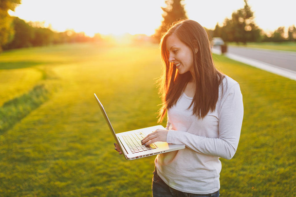 Młody student Kobieta w ubranie. Kobieta siedzi na trawie, ziemi, pracy na komputerze pc, laptop w parku miejskim na zielonej trawie słońce trawnik na zewnątrz. Mobilne biuro. Koncepcja działalności freelancerskiej - Zdjęcie, obraz