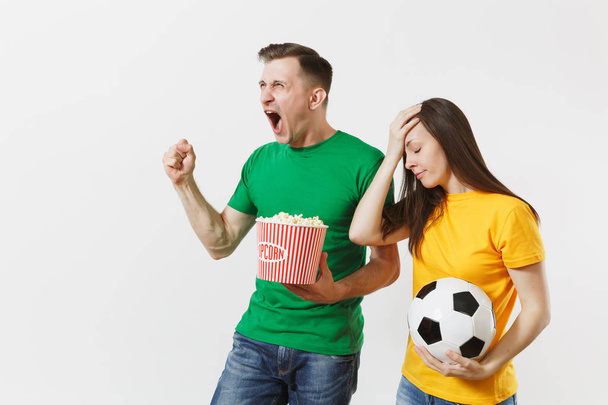 European young couple, woman, man, football fans in yellow green t-shirt cheer up support team with soccer ball bucket of popcorn isolated on white background. Sport family leisure, lifestyle concept - Fotó, kép
