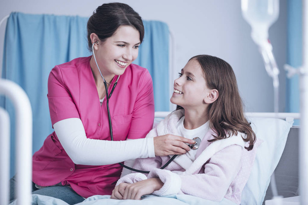 Smiling nurse with stethoscope examining happy girl in the hospital - Foto, imagen