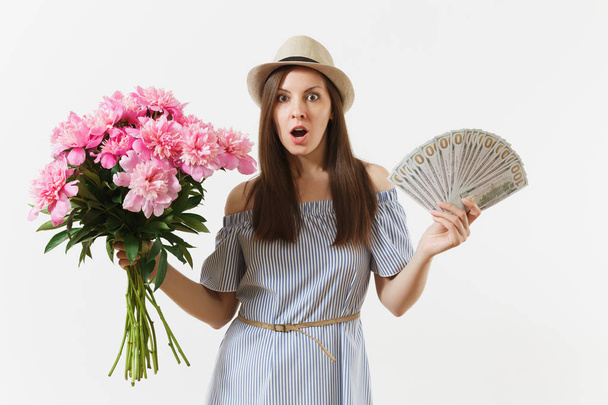 Молодая довольно счастливая женщина в синем платье, шляпа с пачкой долларов, наличные деньги, букет красивых розовых пионов цветы изолированы на белом фоне. Бизнес, доставка, концепция онлайн-шопинга
 - Фото, изображение