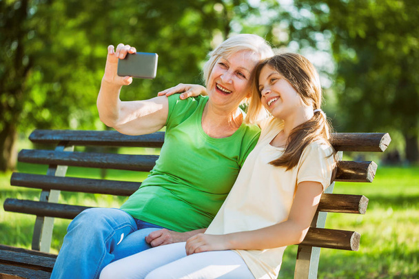 Büyükanne ve torunu parkta oturan ve selfie alarak.  - Fotoğraf, Görsel