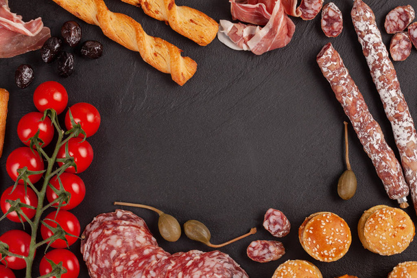 Appetizers table with differents antipasti, cheese, charcuterie, snacks and wine. Mini burgers, sausage, ham, tapas, olives, cheese variety board and baguette over grey concrete background. Top view, flat lay - Photo, image