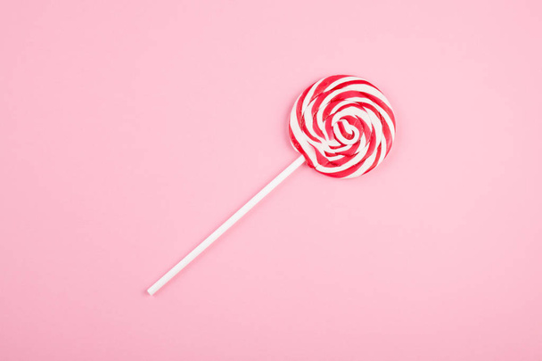 Red and white striped sweet lollipop over the pink background - Zdjęcie, obraz