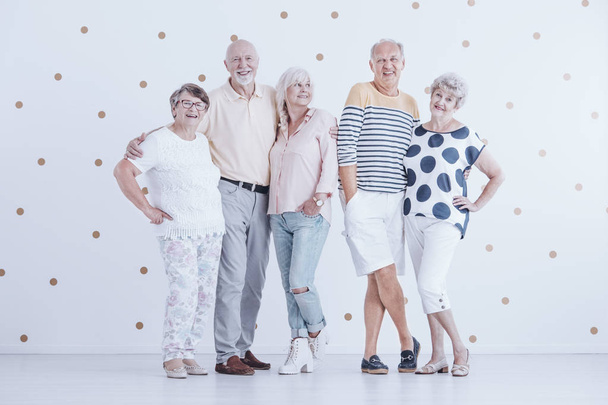 Happy senior couples enjoying meeting against white wall with gold dots - Фото, изображение
