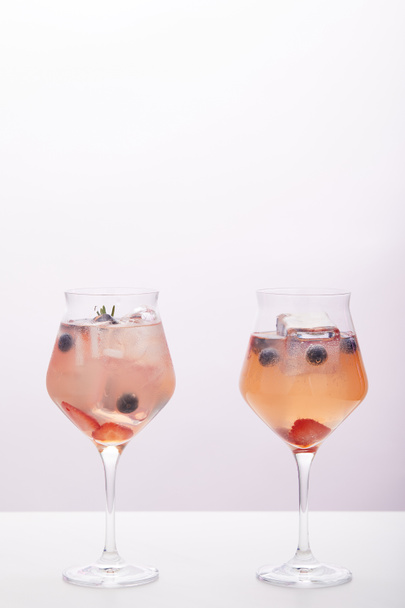 dwie szklanki lemoniady z kostek lodu, rozmaryn, truskawki i jagody na białym tle na szarym tle  - Zdjęcie, obraz