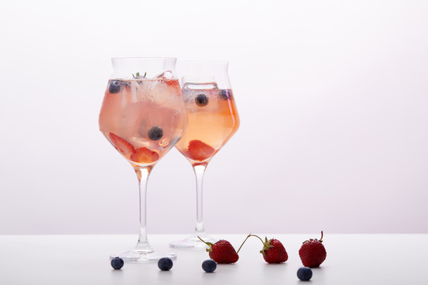 two glasses of lemonade with ice cubes, rosemary, strawberries and blueberries isolated on grey background  - Photo, image