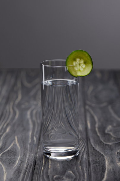 склянка води з шматочком огірка на сірому фоні
  - Фото, зображення