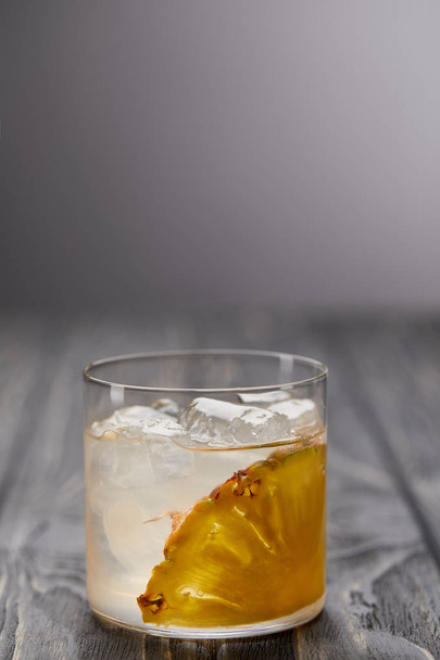 склянка лимонаду з ананасовим шматочком і кубиками льоду на сірому дерев'яному столі
 - Фото, зображення