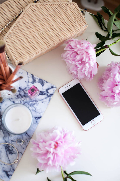 Peonies. Bouquet of pink peonies, candle, wicker bag, scarf, perfume, jewelry, phone on white table Dressing table Spring Cozy - Foto, imagen