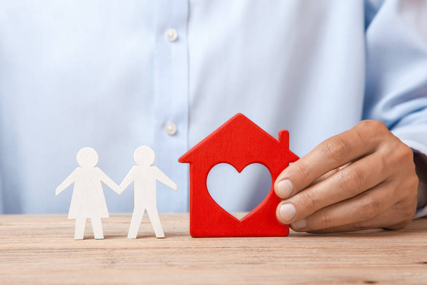 das Konzept der Vermietung eines Eigenheims, eines Kredits oder einer Versicherung. Mann im Hemd hält Haus und Familie steht daneben  - Foto, Bild