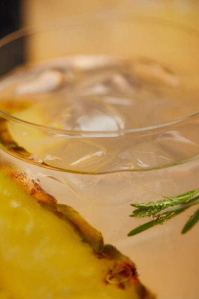 selective focus of glass of lemonade with ice cubes, pineapple pieces and rosemary - Valokuva, kuva