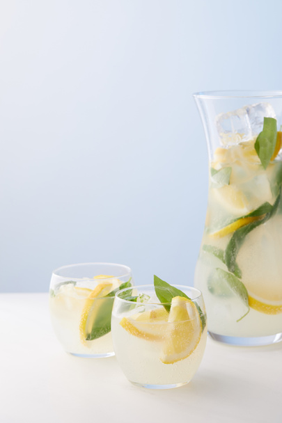  jug and two glasses of lemonade with mint leaves, ice cubes and lemon slices on blue background  - Foto, Imagem