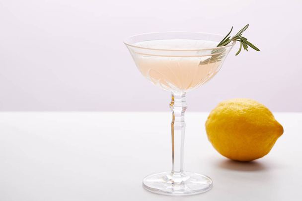 glass of cocktail with rosemary and lemon on purple background  - 写真・画像