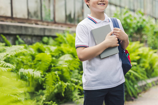 cropped shot of schoolboy with backpack and book in garden - Fotoğraf, Görsel