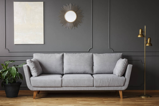 Decorative mirror and modern painting hanging on the wall with molding in dark grey living room interior with fresh plant, gold lamp and bright sofa - Fotoğraf, Görsel