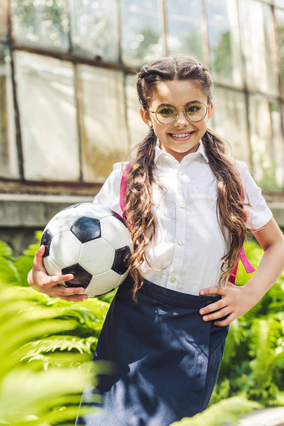 mooie schoolmeisje met voetbal in de tuin kijken naar camera - Foto, afbeelding