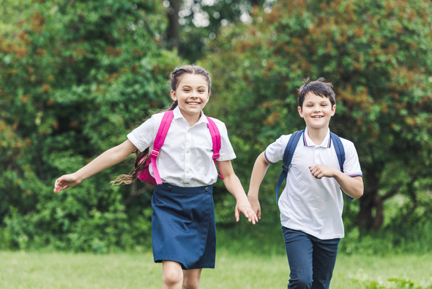 szczęśliwe dzieci w wieku szkolnym z plecakami uruchomiona przez park - Zdjęcie, obraz