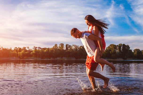 Young man and woman running on summer river bank. Couple in love having fun at sunset. Guys chilling and enjoying freedom - Foto, Imagem