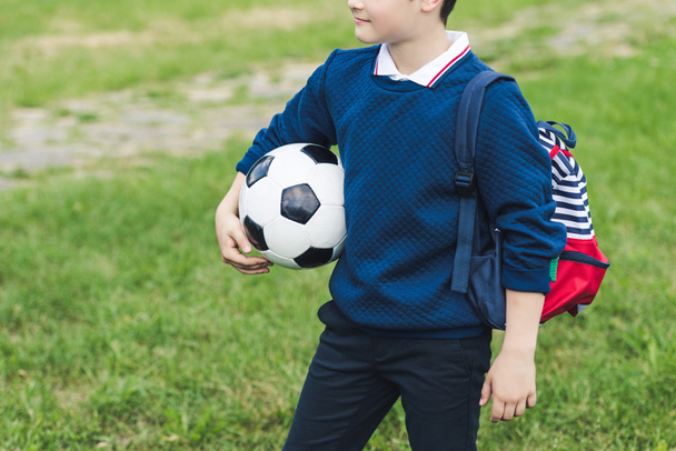cropped shot of kid with soccer ball with soccer ball and backpack on grass field - Fotoğraf, Görsel