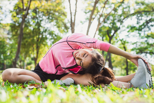 Healthy young asian woman exercising at park. Fit young woman doing training workout in morning. Young happy asian woman stretching at the park after a running workout. Exercise outdoor concept. - Photo, Image