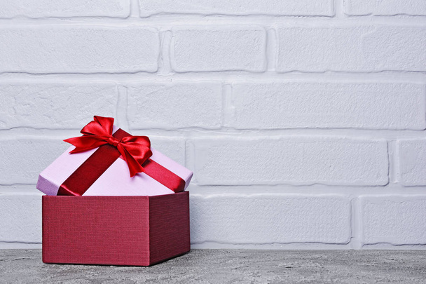 Single purple classic gift box with red satin bow on gray concrete and brick wall background - Fotoğraf, Görsel