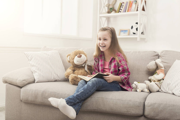 Счастливая маленькая девочка читает книгу для своего плюшевого мишки
 - Фото, изображение