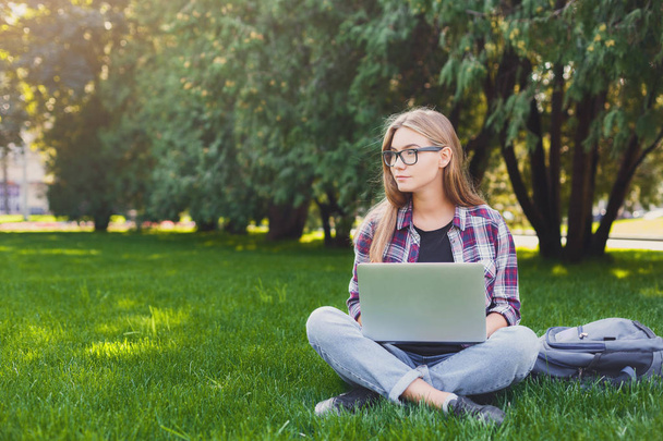 Thoughtful young woman using laptop in park - Zdjęcie, obraz