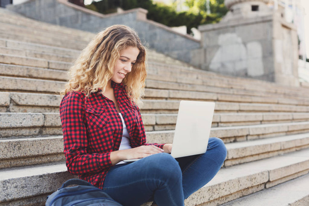 Uśmiechnięta dziewczyna student siedząc na schodach przy użyciu laptopa na zewnątrz - Zdjęcie, obraz