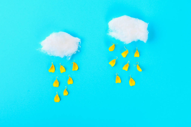Clouds of cotton wool and rain from the petals of a yellow flower on a pastel blue background - Foto, Imagem