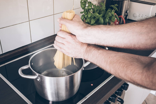 hands putting spaghetti in pot with boiling water on stove - Foto, afbeelding