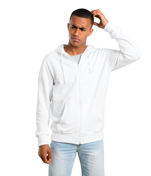 Dark-skinned young man with white sweatshirt having doubts and with confuse face expression while scratching head on isolated white background - Фото, зображення