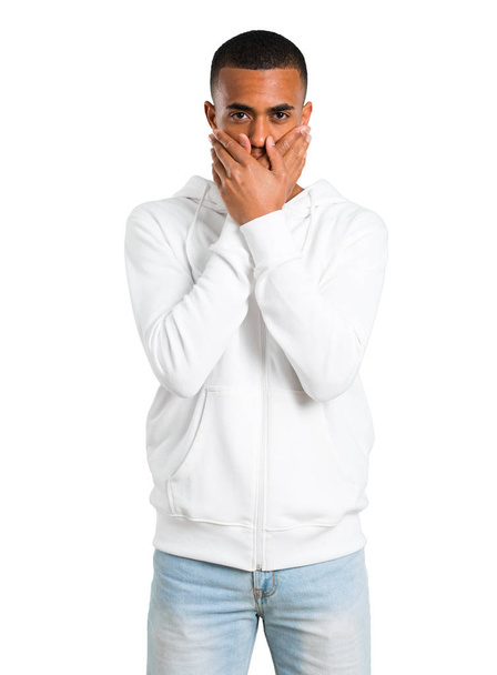 Dark-skinned young man with white sweatshirt covering mouth with both hands for saying something inappropriate. Can not speak on isolated white background - Foto, Imagem