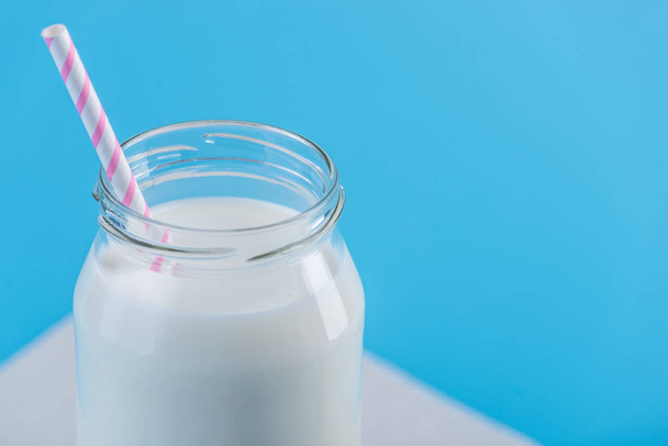 Botella de vidrio de leche fresca con paja sobre fondo azul. Minimalismo colorido. El concepto de productos lácteos saludables con calcio
 - Foto, Imagen