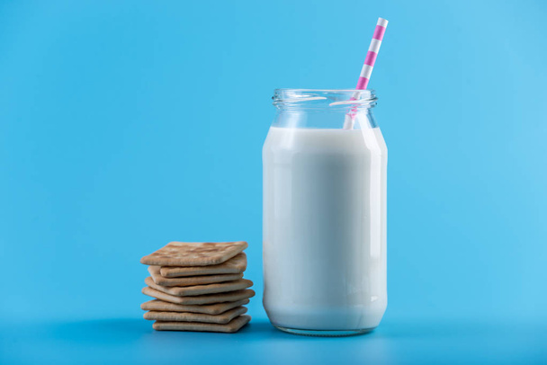 Glasflasche mit frischer Milch mit Stroh und Keksen auf blauem Hintergrund. bunter Minimalismus. das Konzept gesunder Milchprodukte mit Kalzium - Foto, Bild