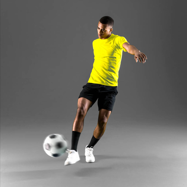Jugador de fútbol hombre con piel oscura jugando patear la pelota sobre fondo oscuro
 - Foto, Imagen