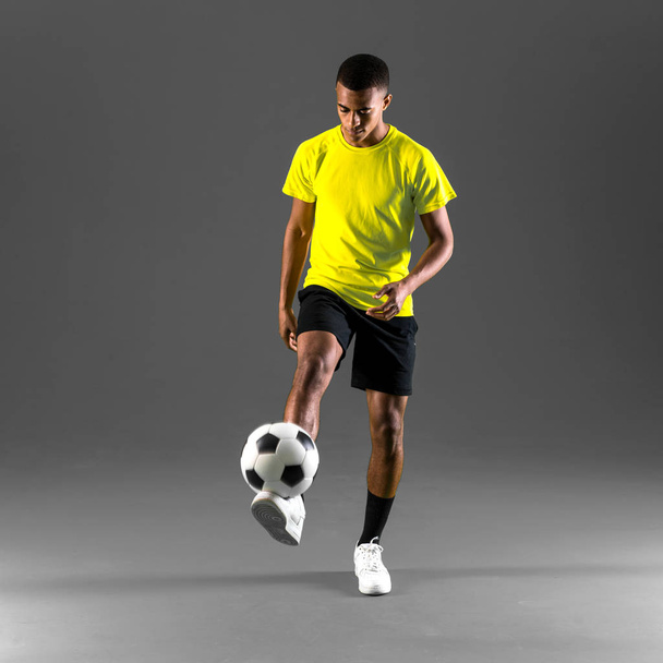 Jogador de futebol homem com pele escura jogando chutando a bola no fundo escuro
 - Foto, Imagem